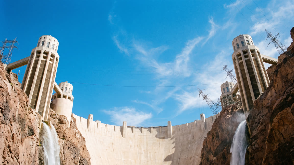 Wide angle photograph of Hoover Dam from the base looking up at the concrete arc against a bright Nevada sky