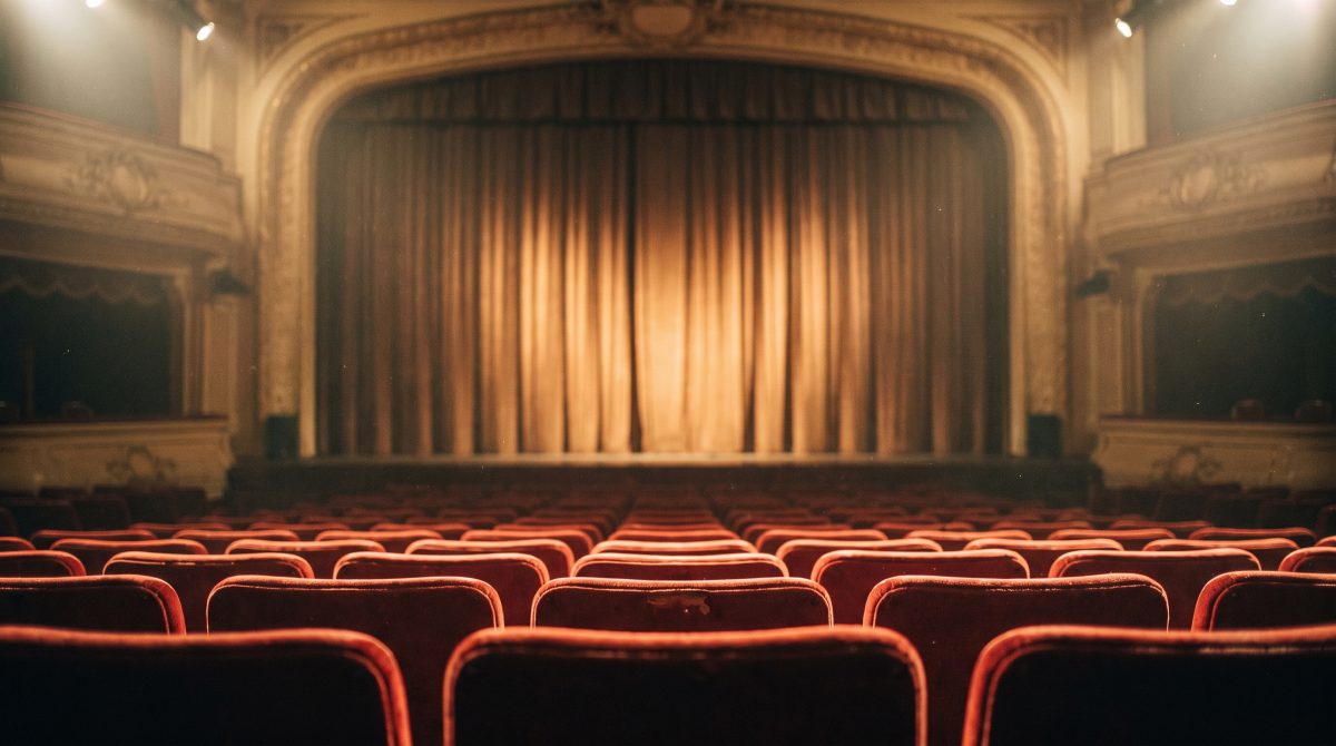 A theatre auditorium before a performance, empty seats facing a lit curtain
